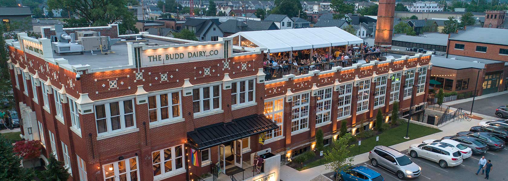 Drone view of Budd Dairy Food Hall showing crowd on rooftop under white tent.