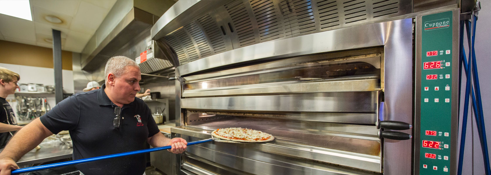 Ed Bisconti, owner of Borgata Pizza Cafe sliding a pizza on a peel into a large metal pizza oven.