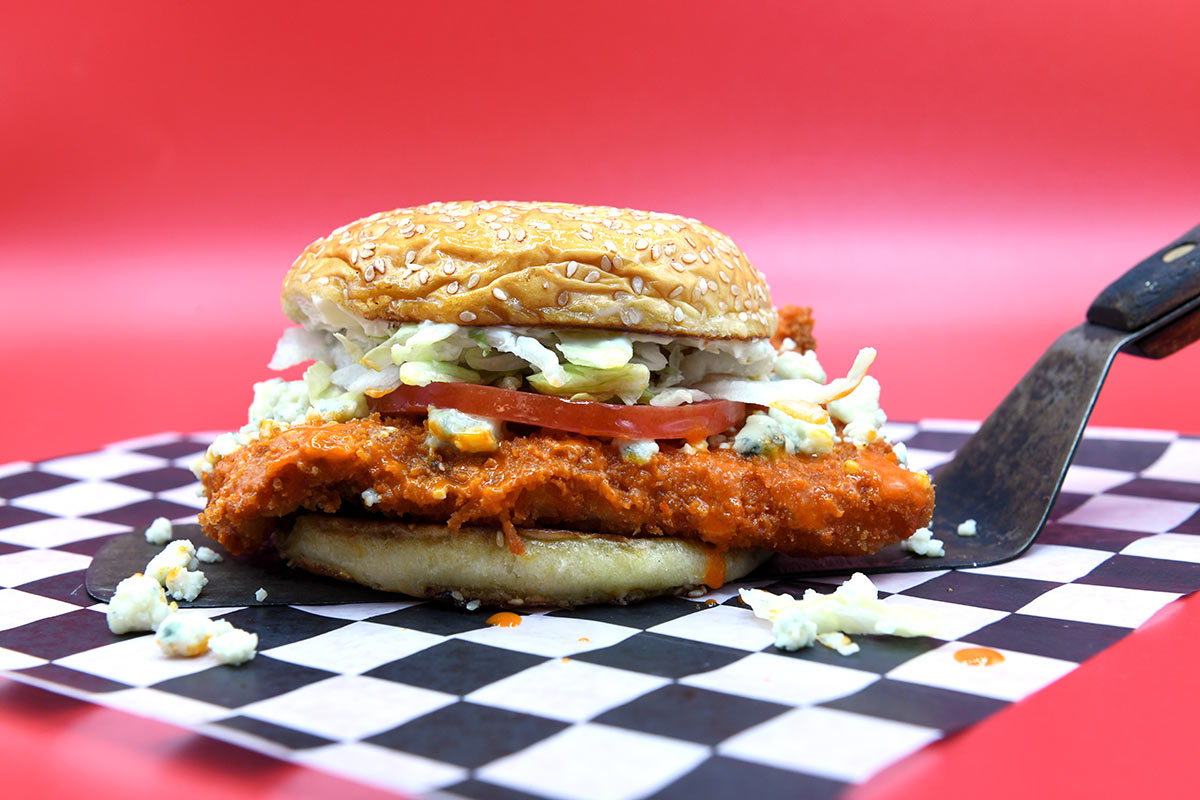 Cluck Norris fried Buffalo Soldier chicken sandwich with lettuce and tomato garnish sitting on spatula