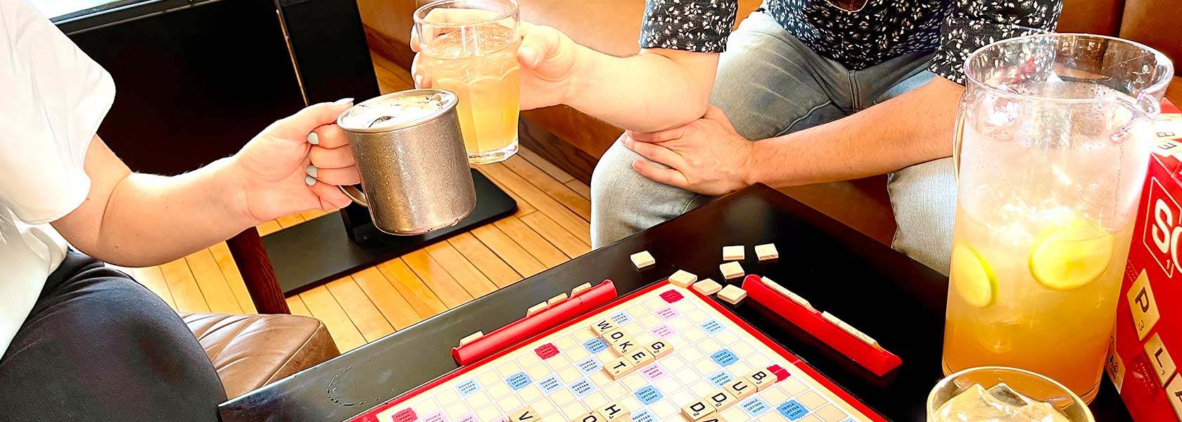 Hands toasting glasses of happy hour beverages over Scrabble gamer board