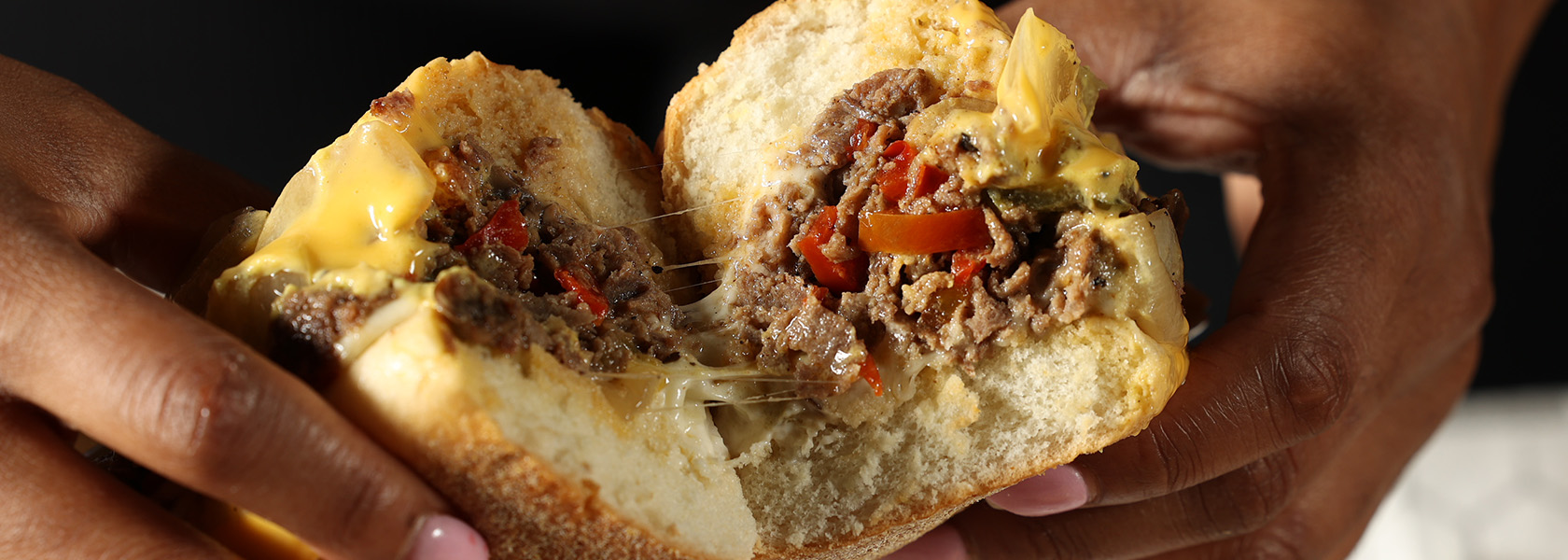 Hands holding cut Marlow's Cheesesteaks sandwich.